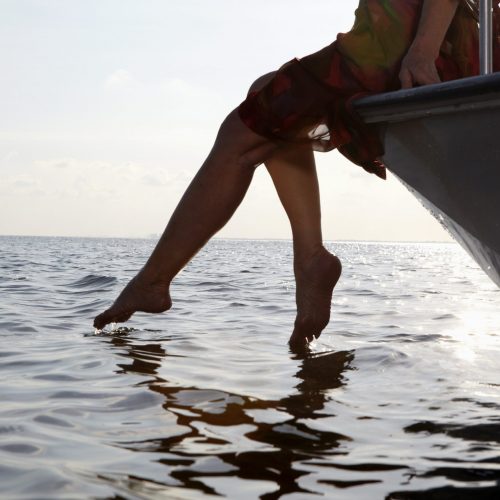 Senior woman sitting on edge of motorboat with feet in water