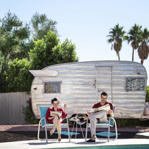 Couple Reading Newspaper While Sitting On Chair Against Camper Van